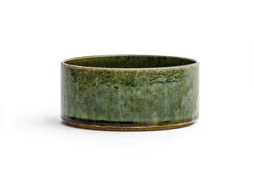 Silhouetted image of small ceramic oribe bowl with deep green glaze by Time and Style against white background.