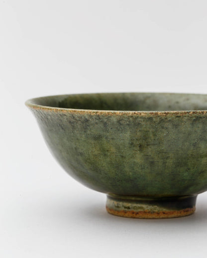 Cropped image of ceramic oribe rice bowl with deep green glaze by Time and Style against white-gray background.
