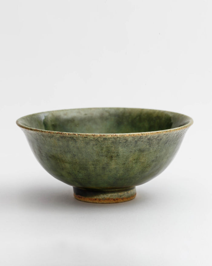 Silhouetted image of ceramic oribe rice bowl with deep green glaze by Time and Style against white-gray background.