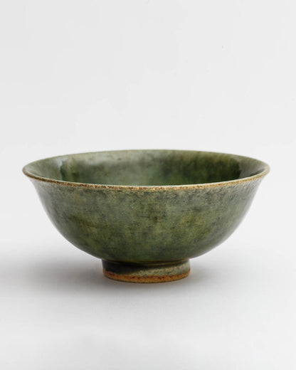 Silhouetted image of ceramic oribe rice bowl with deep green glaze by Time and Style against white-gray background.