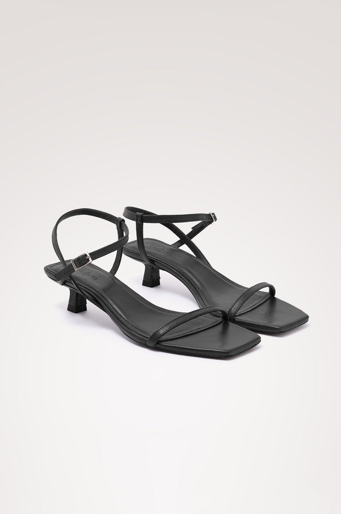 Palma Sandal Heel in Top-Grain Leather With Single Toe Strap, Adjustable Buckled Wrap Ankle Strap, and Low Heel in Black Colorway - angeled frontview of shoe.