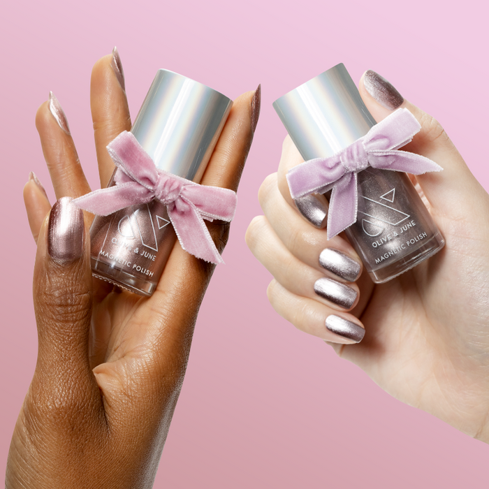Two hands holding Pretty Neutral Velvet Duo bottles with velvet bows and matching manicured nails against pink background