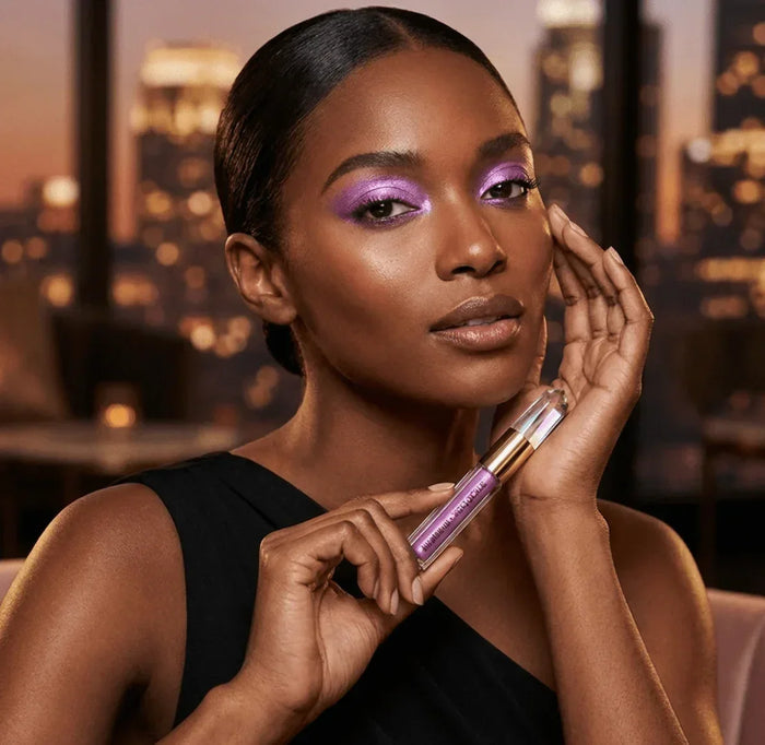 Woman wearing purple shimmer eyeshadow holding matching tube, glam beauty makeup look
