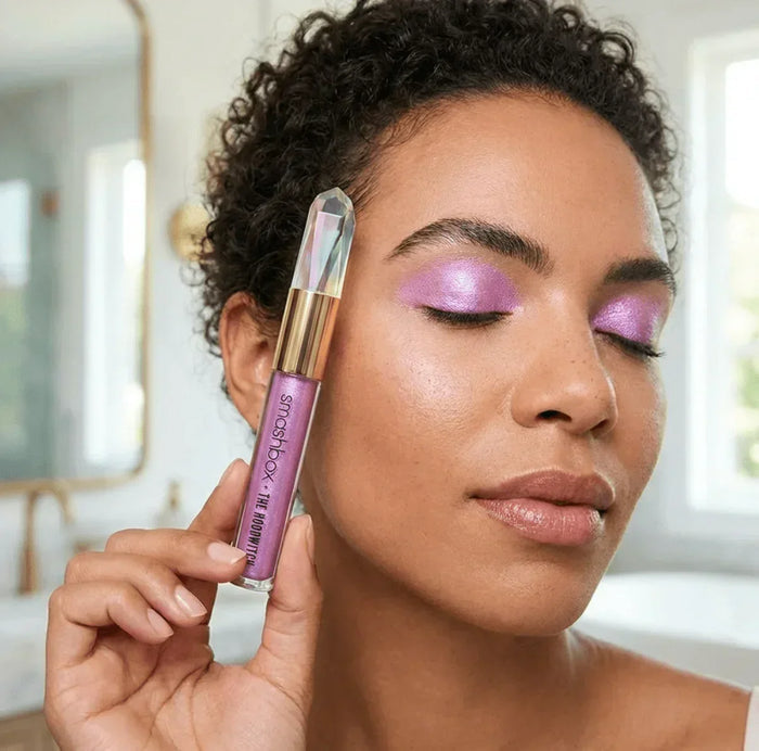 Woman wearing shimmery pink eyeshadow holding Smashbox shimmer eyeshadow in bright room