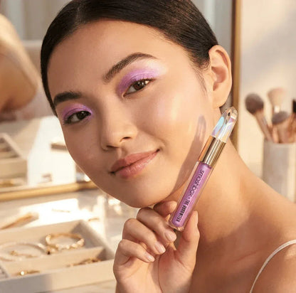 Woman with shimmering purple eyeshadow holding Smashbox makeup in a bright vanity setting