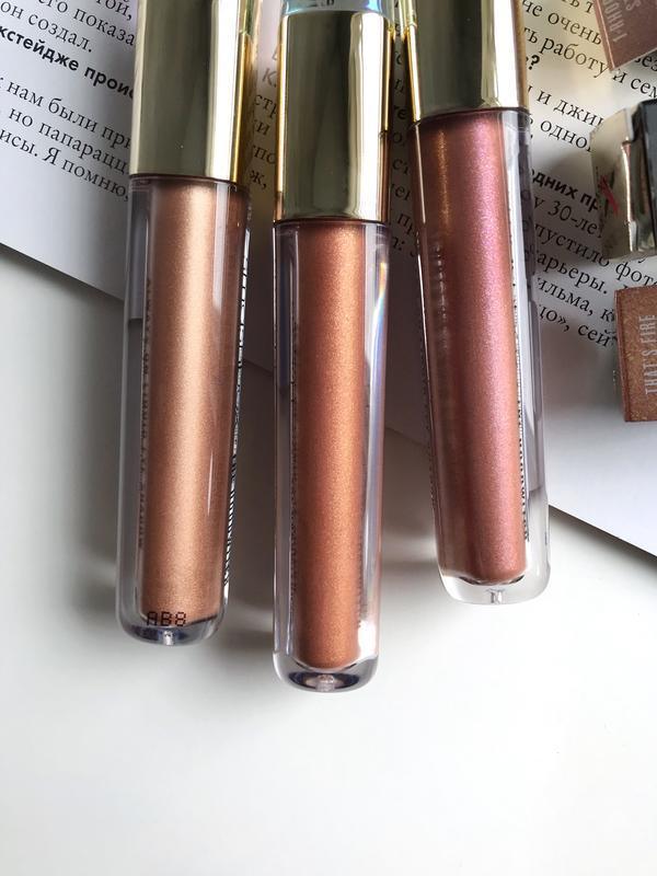 Three tubes of pink and bronze shimmer liquid eyeshadow with gold caps on a white surface
