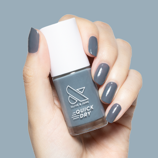 Hand holding Olive and June Torrential quick-dry gel polish bottle with matching moody slate grey manicure on short nails
