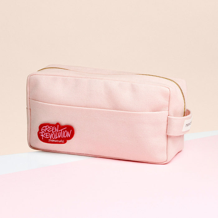 The Manucurist-us Ultimate Pink Bag is a light pink rectangular pouch with a front pocket and a red "Green Revolution" patch. It’s perfect for storing your Green Flash kit essentials, photographed on a pink and white surface with a beige background.