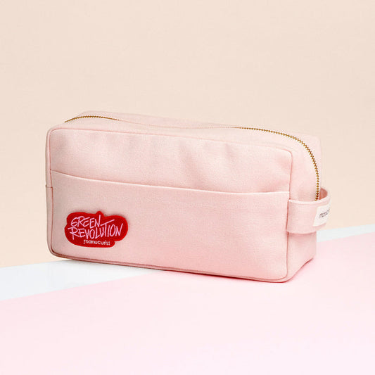 The Manucurist-us Ultimate Pink Bag is a light pink rectangular pouch with a front pocket and a red "Green Revolution" patch. It’s perfect for storing your Green Flash kit essentials, photographed on a pink and white surface with a beige background.