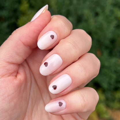Vampy Heart - Press-On | Medium | Oval hand with medium oval false nails in pale polish accented with small dark heart details manicure