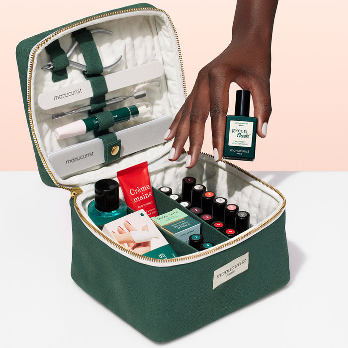 The Manucurist-test Vanity Case is a green manicure kit with nail care tools, polishes, hand cream, and accessories in a zippered pouch—a compact organizer. A hand holds a “green flash” polish.